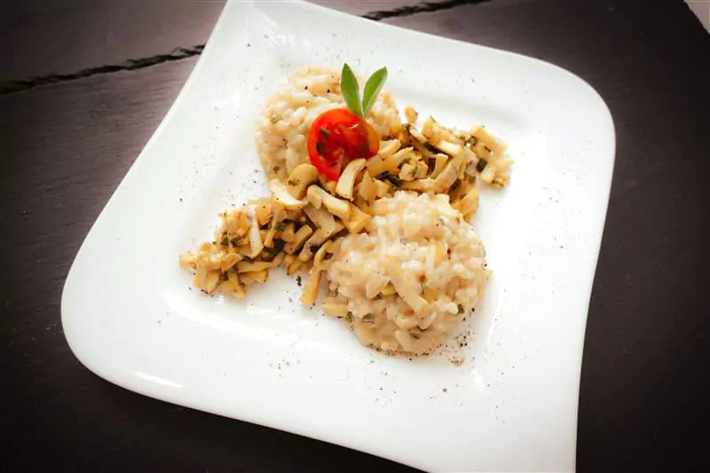 Pilzrisotto mit Reis auf einem Teller, mit Tomate garniert.